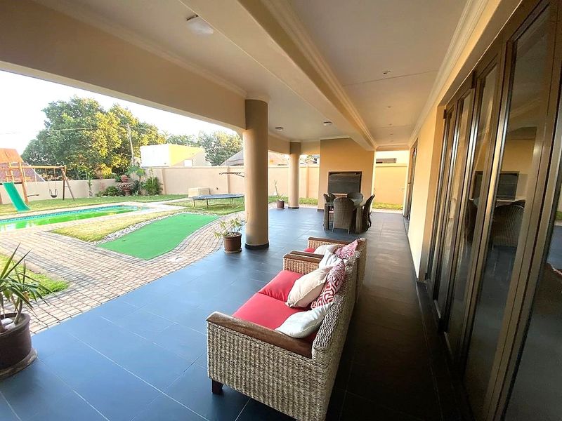 Spacious covered patio featuring tiled flooring, recessed lighting, and a built-in braai, offering seamless indoor-outdoor flow to the garden and pool area.
