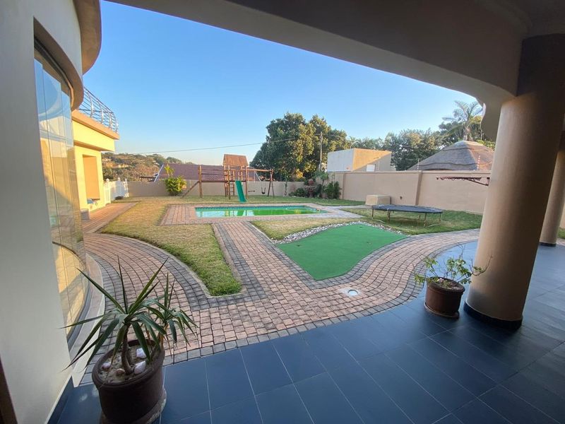 A spacious covered patio overlooking a landscaped garden featuring a swimming pool, paved walkways, and a secure boundary wall.