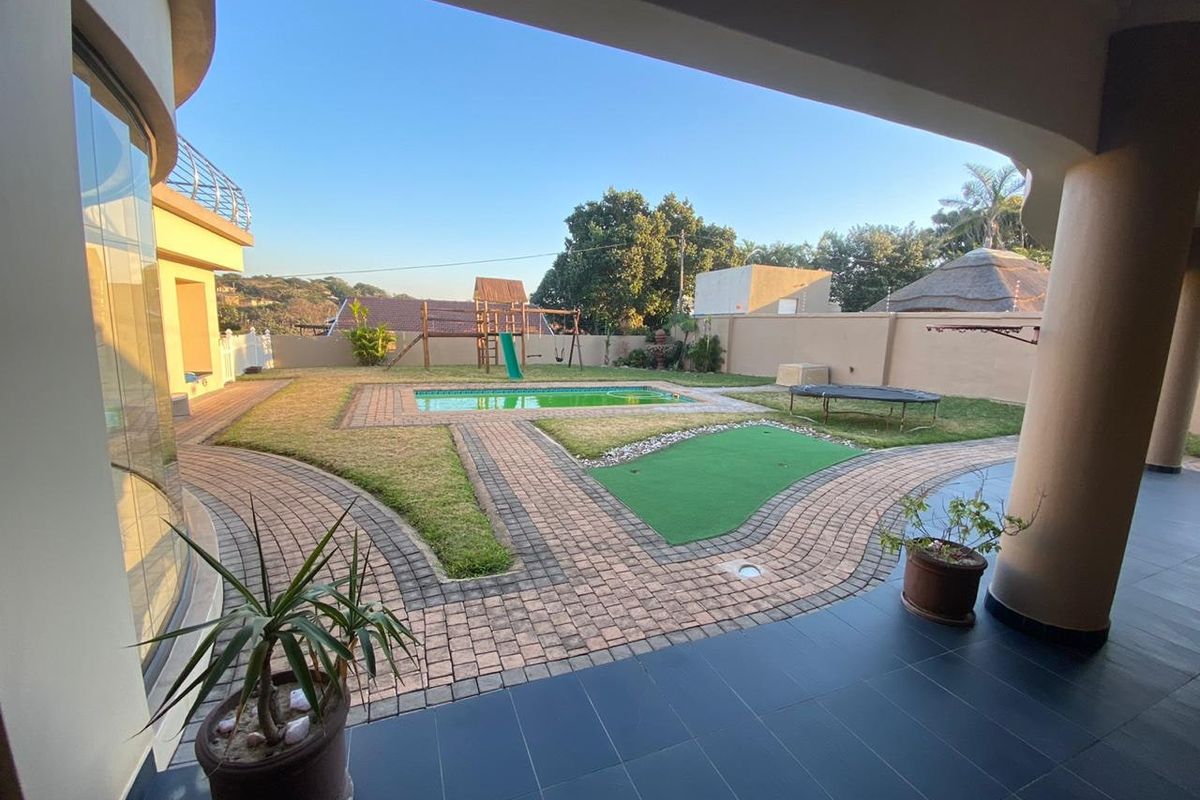 A spacious covered patio overlooking a landscaped garden featuring a swimming pool, paved walkways, and a secure boundary wall.