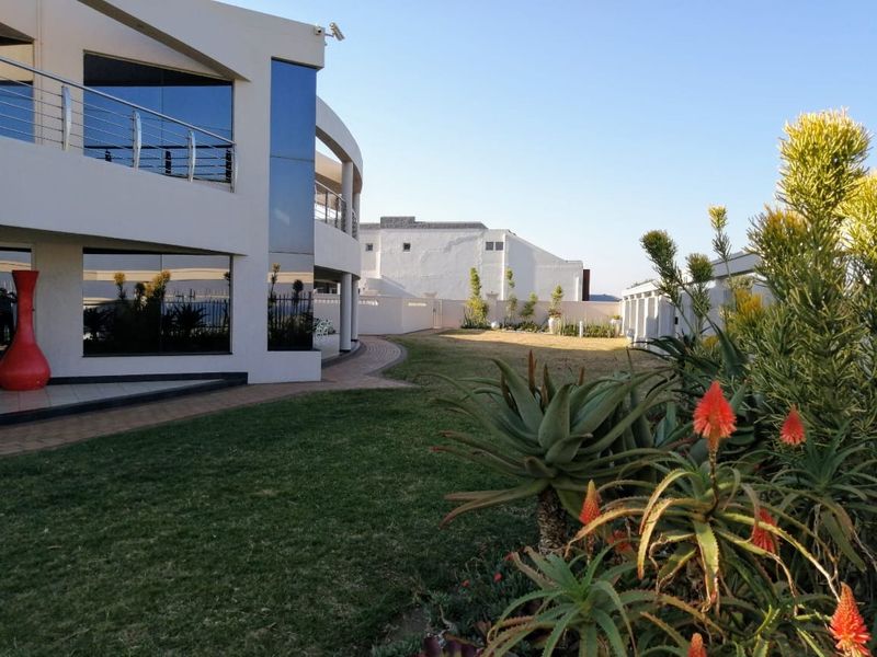 A well-maintained rear garden featuring a paved walkway, landscaped lawn, and a modern multi-story building with a balcony and stainless steel balustrades.