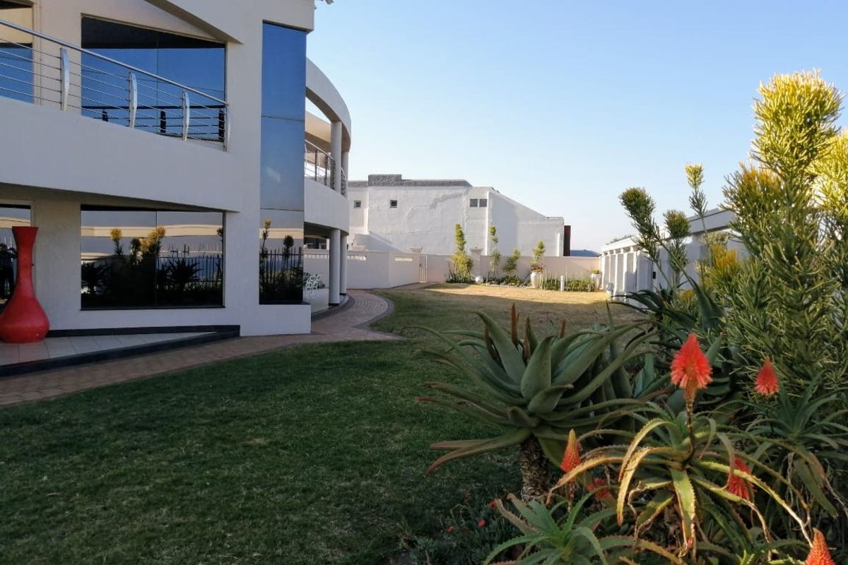 A well-maintained rear garden featuring a paved walkway, landscaped lawn, and a modern multi-story building with a balcony and stainless steel balustrades.