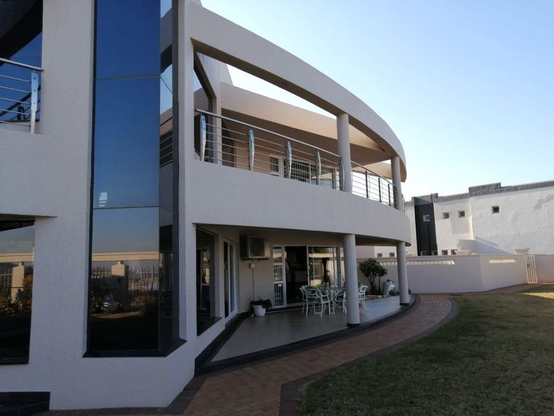 Rear view of a modern multi-story home featuring a curved balcony with stainless steel railings, a tiled patio, and a paved garden walkway.