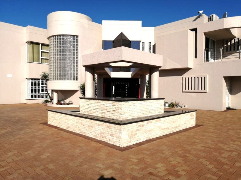 Front elevation of a modern residence featuring a paved driveway, a central stone-clad water feature, and distinctive architectural glass block detailing.