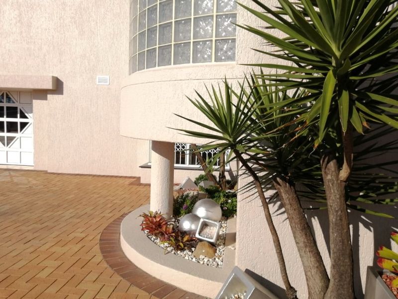 Front exterior view featuring a textured facade, curved glass block window, and brick paved driveway with a built-in concrete planter.