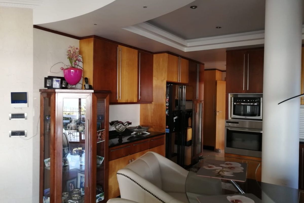 A well-appointed kitchen featuring warm-toned wooden cabinetry, granite countertops, and integrated appliances, complemented by a modern bulkhead ceiling design.