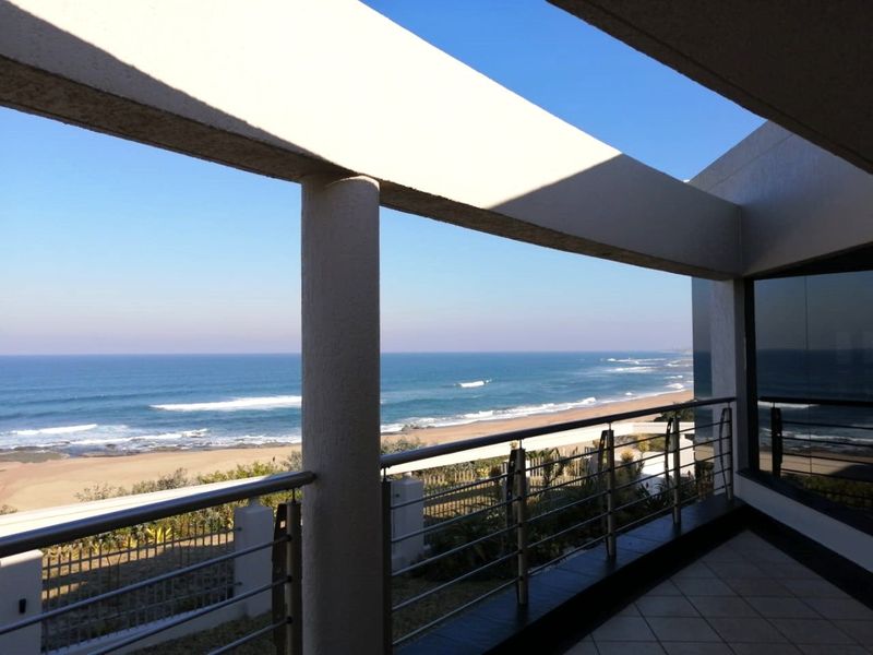 Spacious covered balcony featuring tiled flooring and a stainless steel balustrade, offering expansive, unobstructed views of the coastline and ocean.