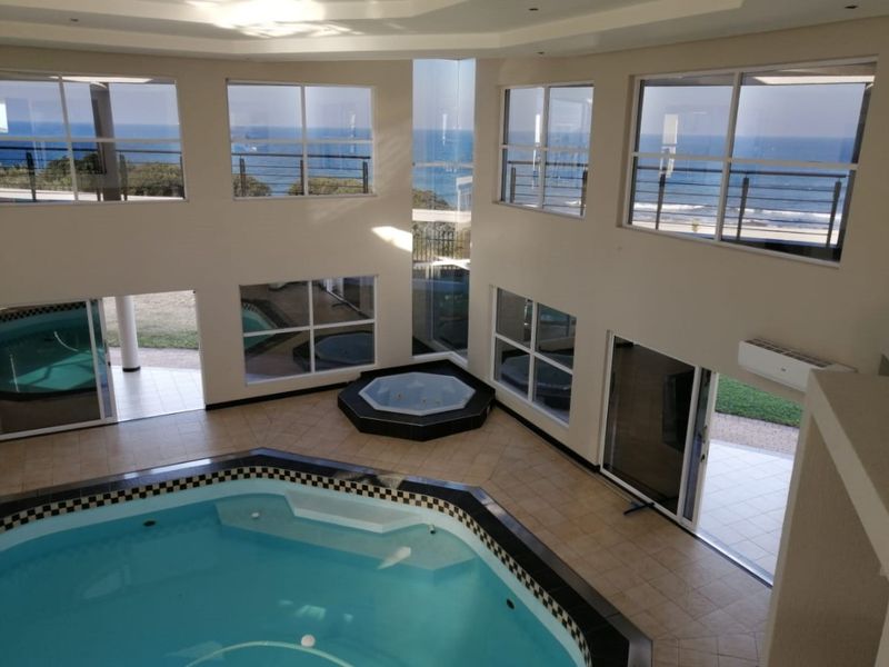 Spacious indoor pool area featuring a built-in swimming pool, integrated jacuzzi, and expansive windows offering panoramic ocean views.