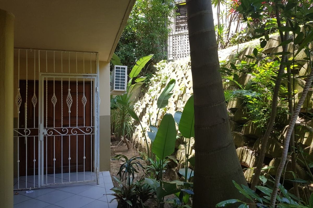 A rear exterior view featuring a tiled patio area, security gate, and a landscaped retaining wall with established greenery.