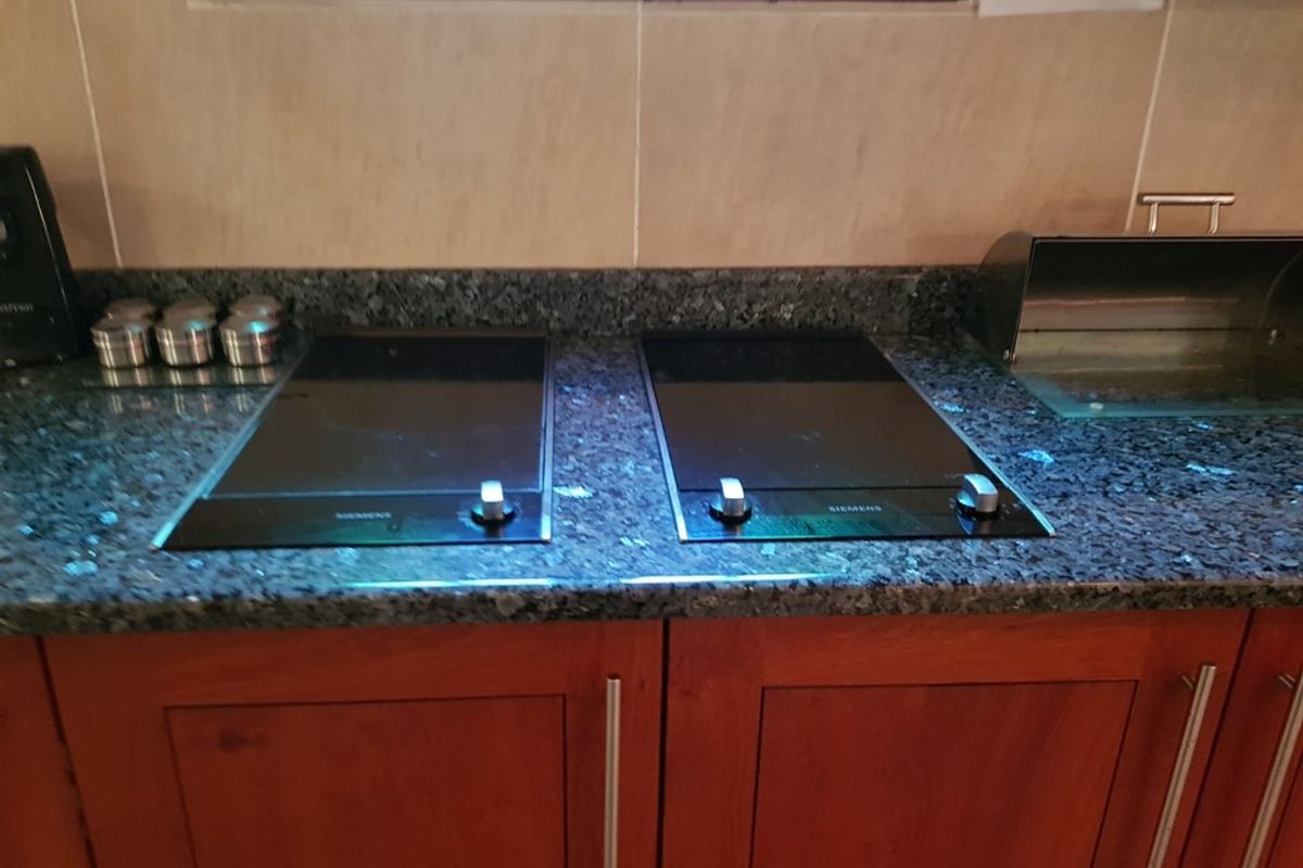 A kitchen workspace featuring granite countertops, dual built-in induction hobs, and wooden cabinetry with a tiled backsplash.