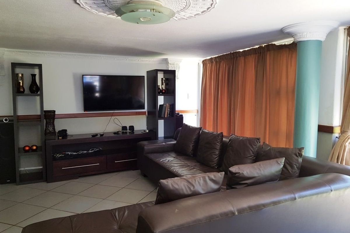 Spacious living room featuring decorative ceiling rose, coving, and a structural column, finished with tiled flooring.