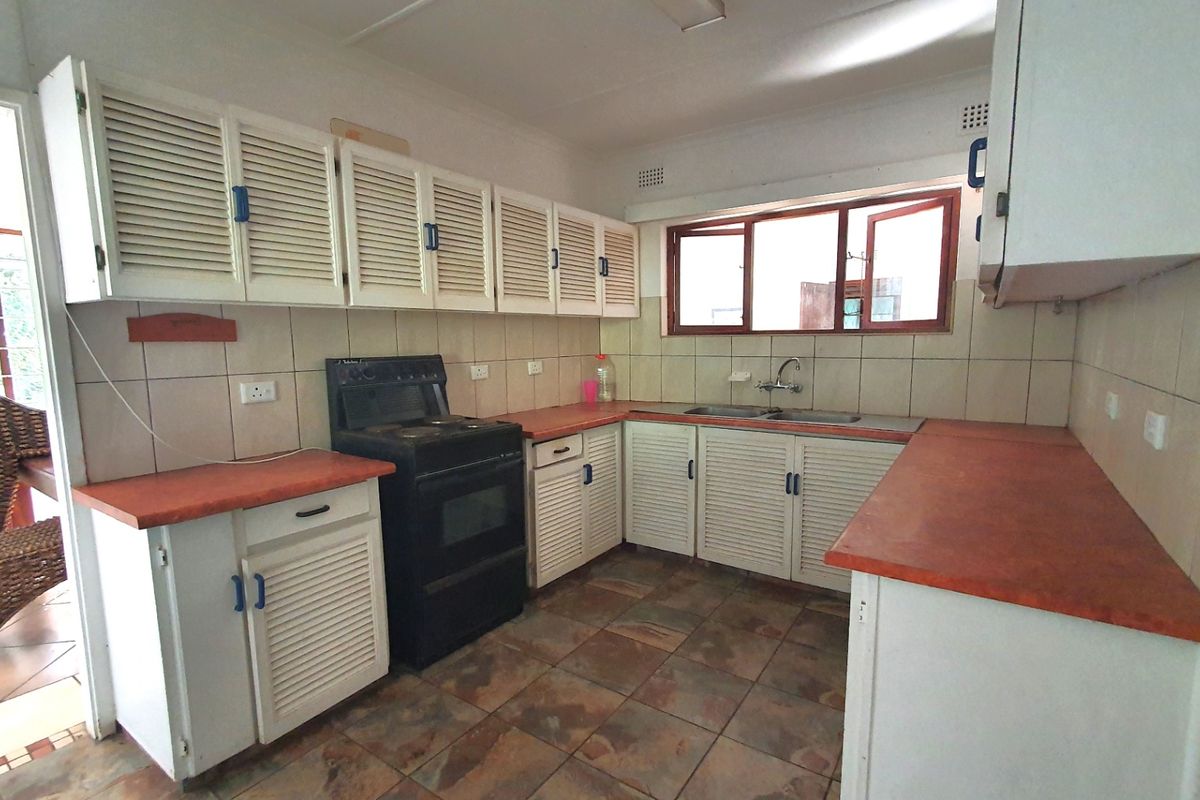 A functional kitchen featuring louvered cabinetry, laminate countertops, a freestanding stove, and tiled flooring, offering potential for a modern renovation.