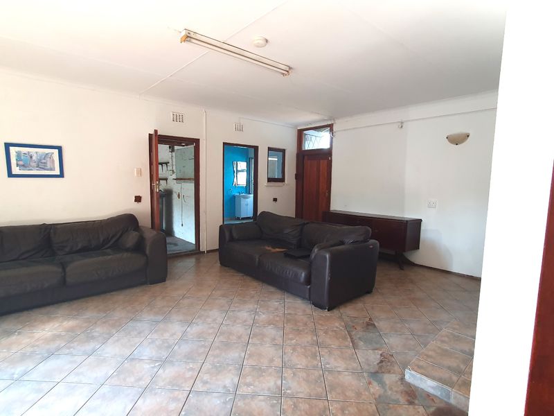 A spacious living area featuring tiled flooring, multiple doorways leading to adjacent rooms, and basic lighting fixtures, offering a blank canvas for renovation.