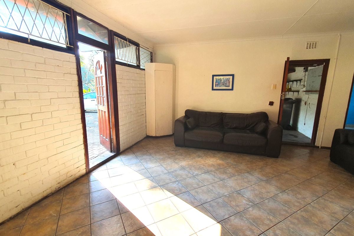 A living room featuring tiled flooring and painted brick walls, with direct access to the exterior and views into adjacent rooms.