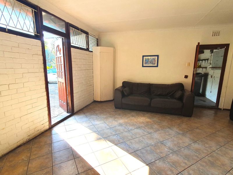 A living room featuring tiled flooring and painted brick walls, with direct access to the exterior and views into adjacent rooms.