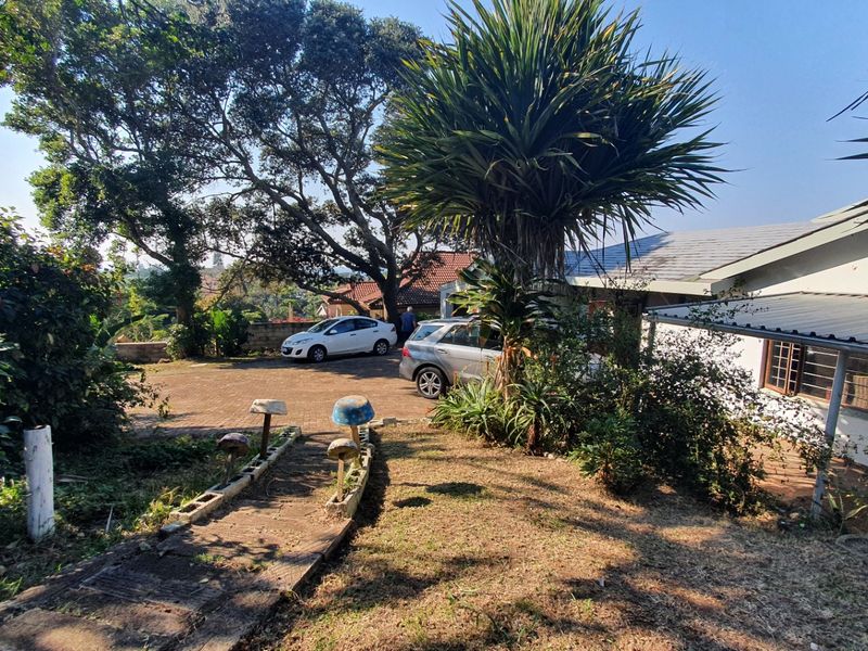 Front exterior view of the property featuring a paved driveway, metal roofing, and a concrete pathway leading to the house entrance.