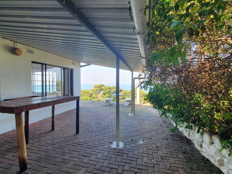 Covered outdoor patio area featuring brick paving, metal roofing, and support columns, offering a view of the surrounding landscape.