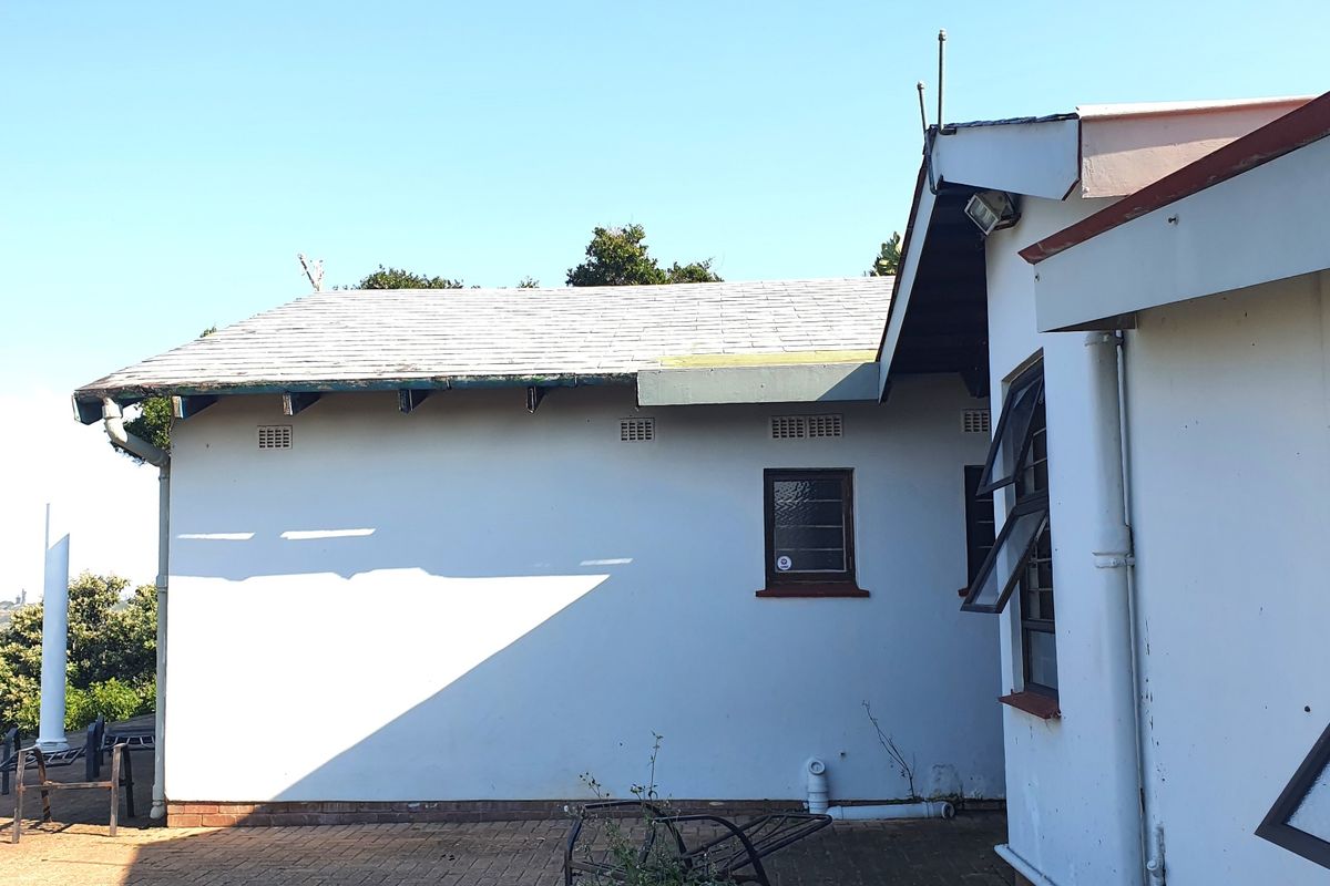 Rear exterior view of the house showing a paved patio area, tiled roof, and casement windows with visible signs of exterior maintenance required.