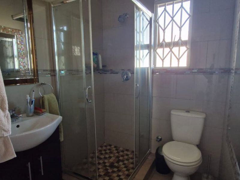 A functional bathroom featuring a glass shower enclosure, vanity cabinet with basin, toilet, and decorative mosaic tile accents on the walls.