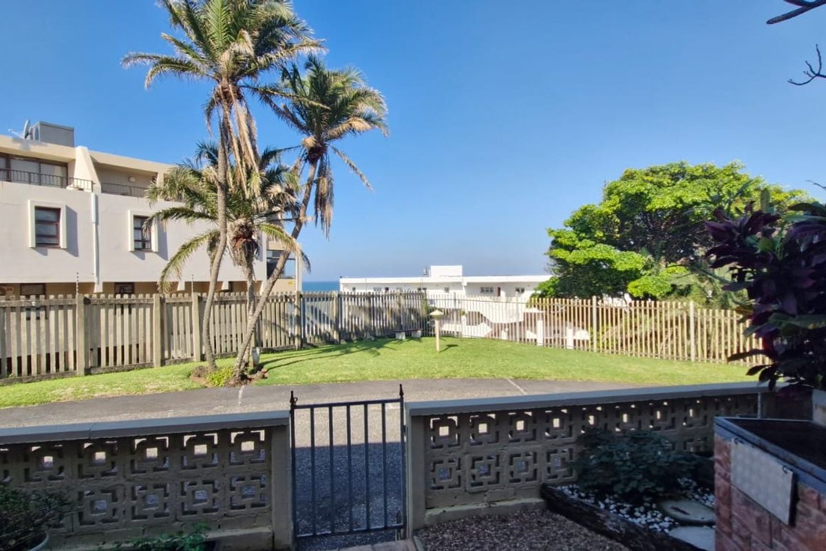 A rear exterior view featuring a private lawn area, brick boundary wall, metal gate, and a built-in brick braai facility.