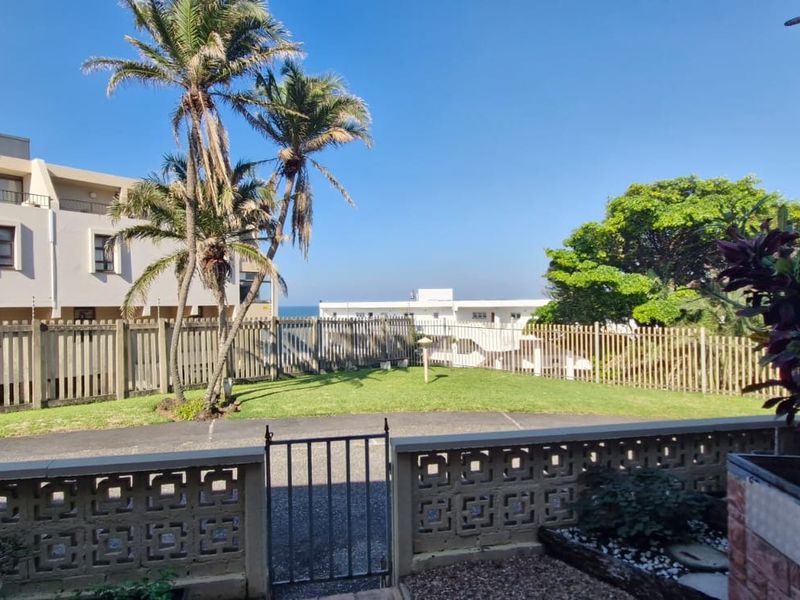 A rear exterior view featuring a private lawn area, brick boundary wall, metal gate, and a built-in brick braai facility.
