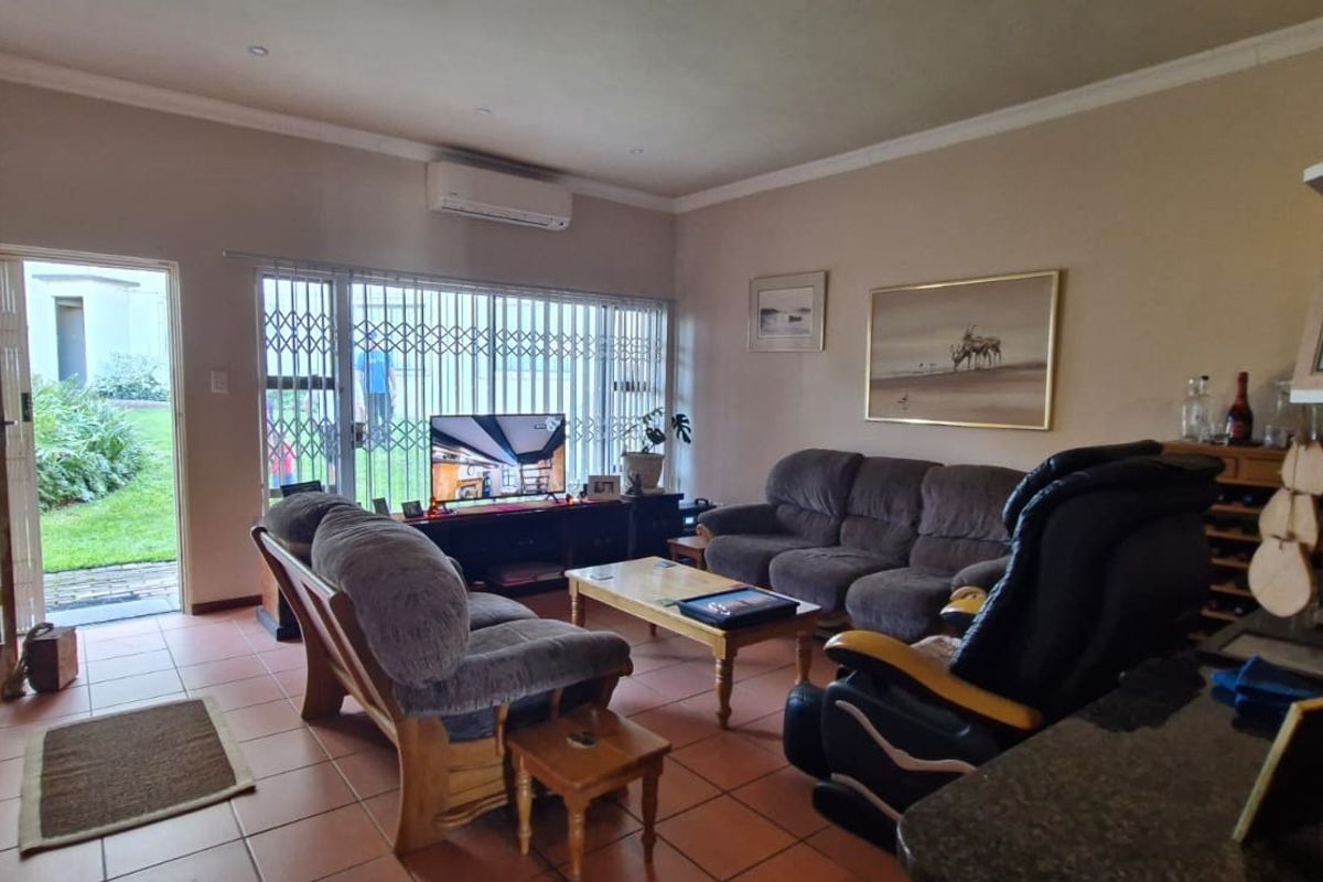 A comfortable living room featuring tiled flooring, a wall-mounted air conditioning unit, and direct access to an outdoor area through a security gate.