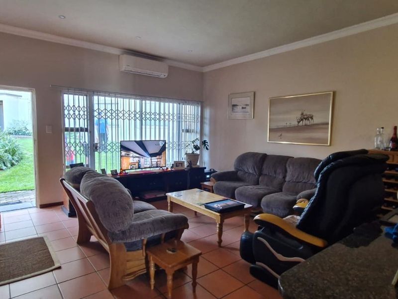 A comfortable living room featuring tiled flooring, a wall-mounted air conditioning unit, and direct access to an outdoor area through a security gate.