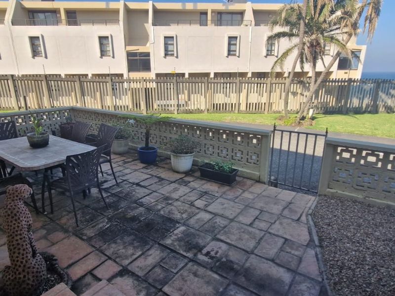 A paved outdoor patio area featuring a decorative concrete block wall, metal gate, and electric fencing, overlooking a shared garden space.