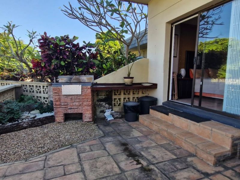 Outdoor patio area featuring a built-in brick braai, tiled flooring, and sliding glass door access to the interior living space.