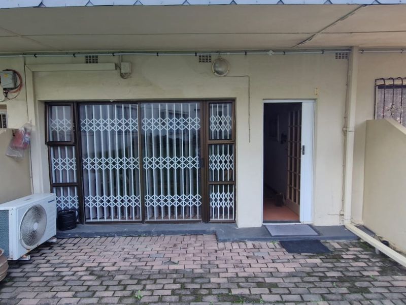 Front entrance area featuring brick paving, a sliding door with security gate, and an external air conditioning unit.