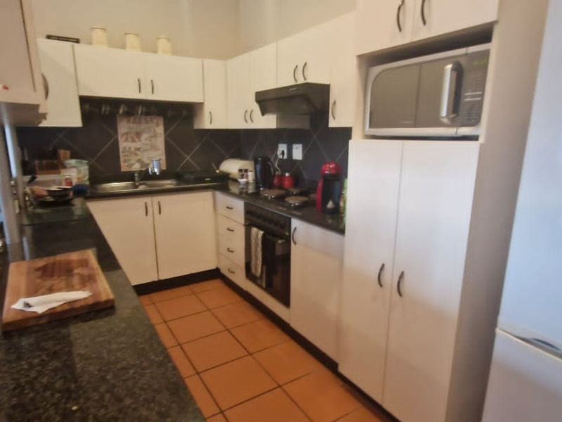 A functional kitchen featuring granite countertops, built-in oven, extractor fan, and ample white cabinetry with tiled flooring.