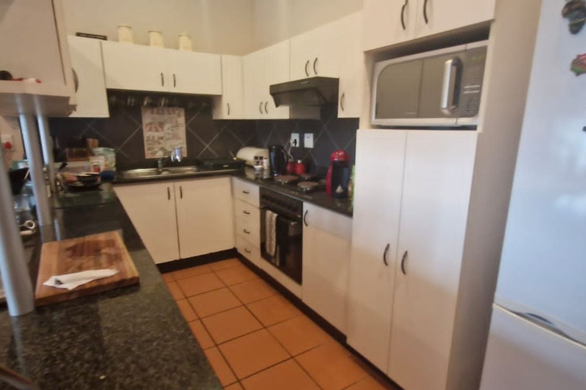A functional kitchen featuring granite countertops, built-in oven, extractor fan, and ample white cabinetry with tiled flooring.