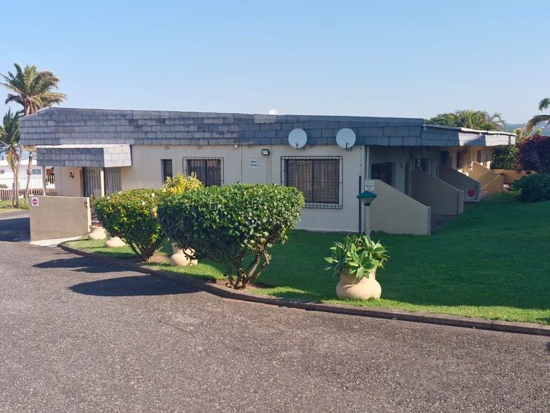 Exterior view of an apartment complex featuring a slate roof, paved driveway, and well-maintained communal lawn area.