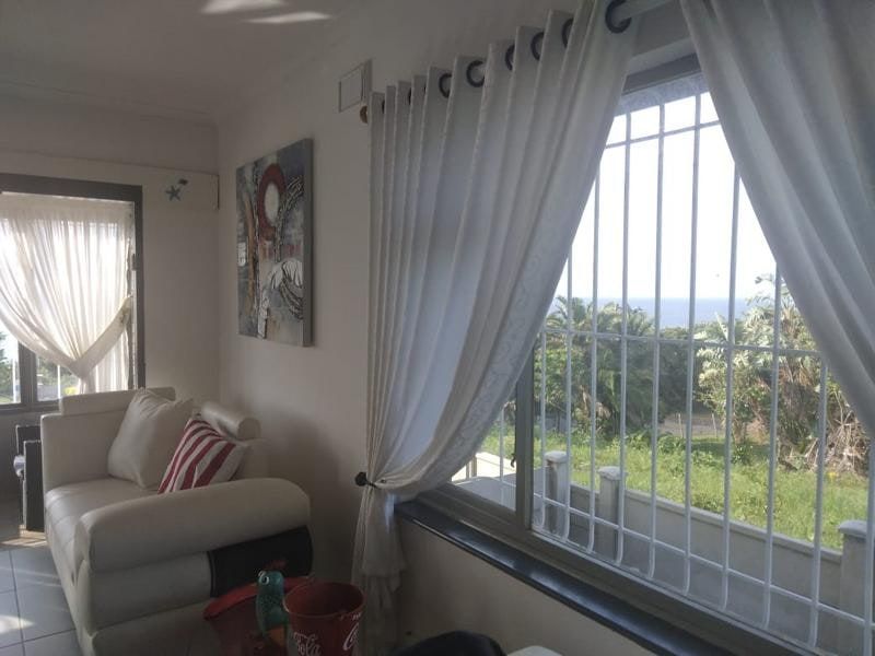 A bright living area featuring large windows with security bars, offering natural light and views of the surrounding greenery.
