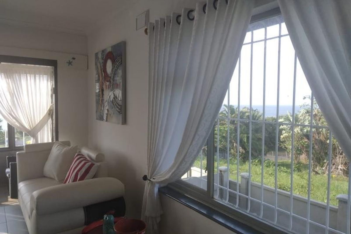 A bright living area featuring large windows with security bars, offering natural light and views of the surrounding greenery.