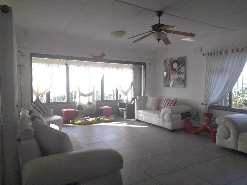 Spacious living room featuring large windows, tiled flooring, and a ceiling fan, offering a bright and open atmosphere.