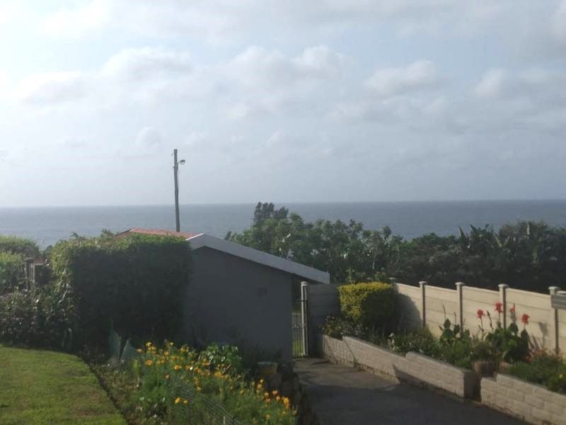 A scenic view of the ocean from the property, featuring a paved driveway, landscaped garden beds, and a precast concrete boundary wall.
