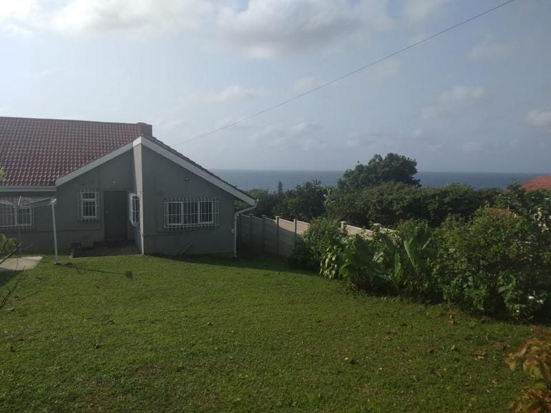 Rear view of the property featuring a spacious lawn, precast boundary wall, and a clear view of the ocean in the distance.