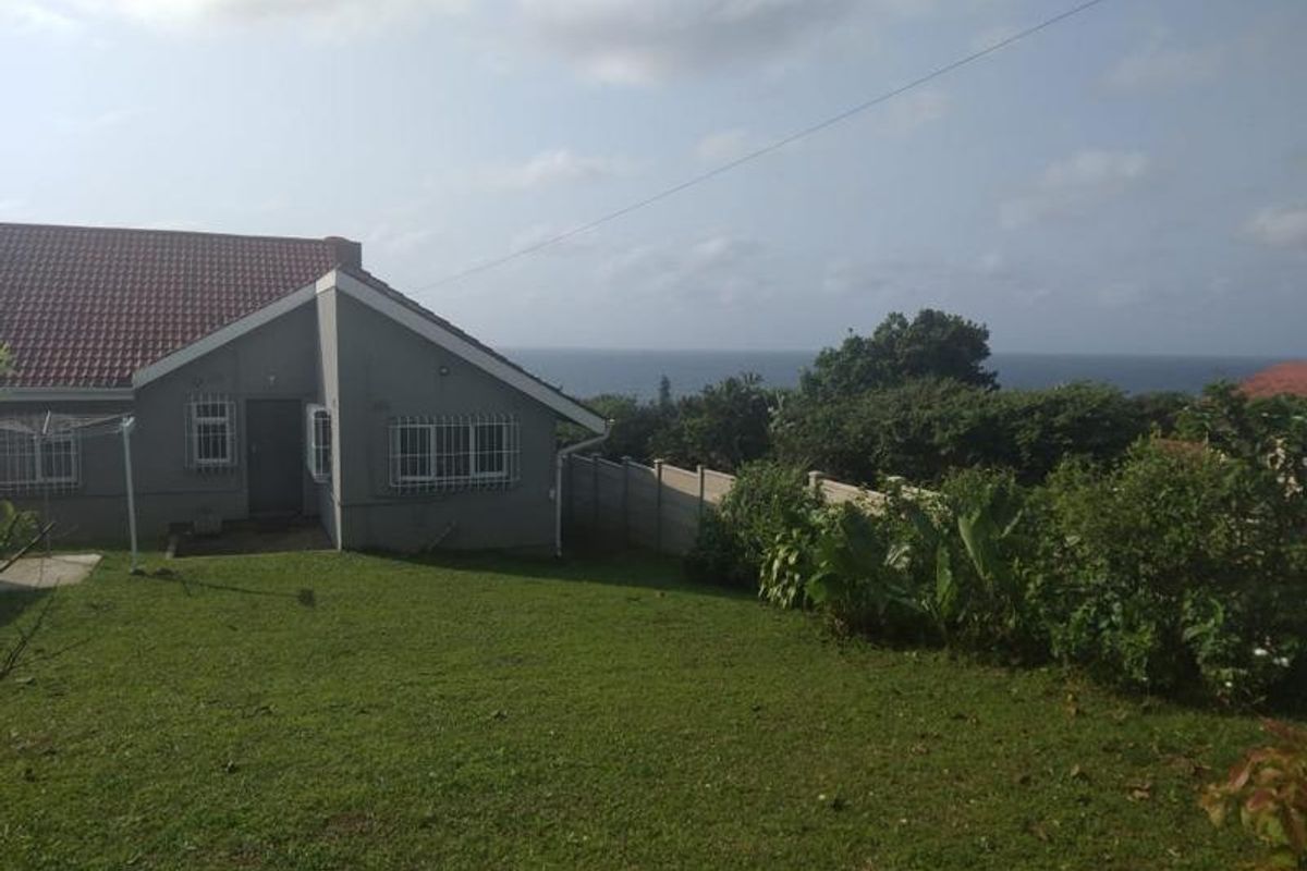 Rear view of the property featuring a spacious lawn, precast boundary wall, and a clear view of the ocean in the distance.