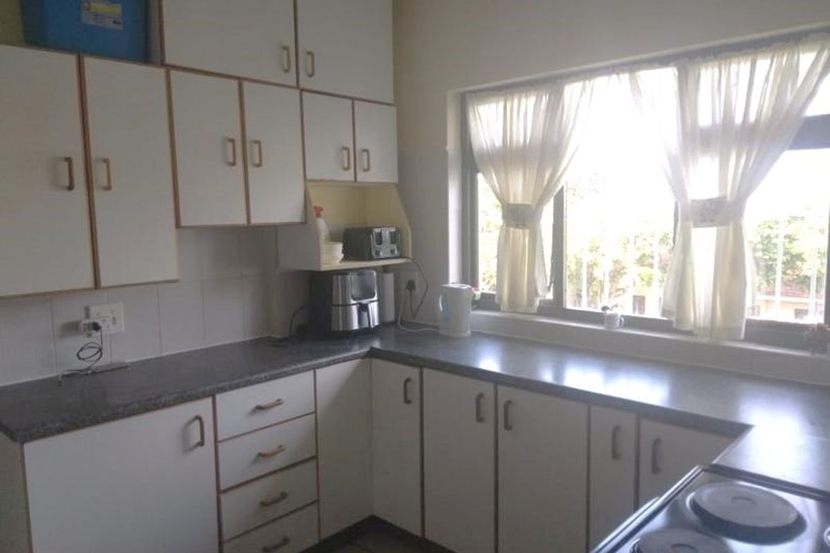 A functional kitchen featuring white cabinetry, laminate countertops, and an electric hob, offering a practical layout with ample storage space.
