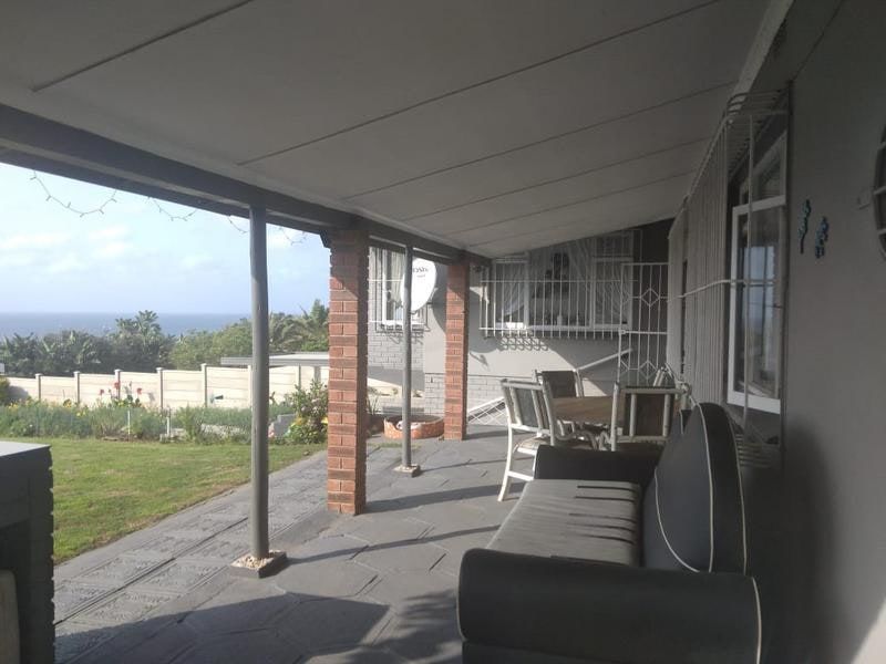 A covered outdoor patio area featuring brick pillars and paved flooring, offering views of the surrounding garden and distant ocean.