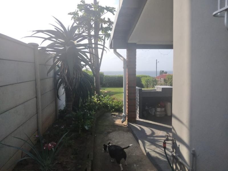 A covered patio area featuring a built-in braai, overlooking a garden with distant sea views.
