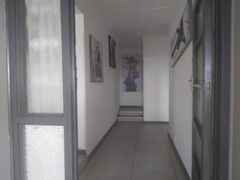 A neutral hallway featuring tiled flooring and grey door frames, leading towards a small set of steps.