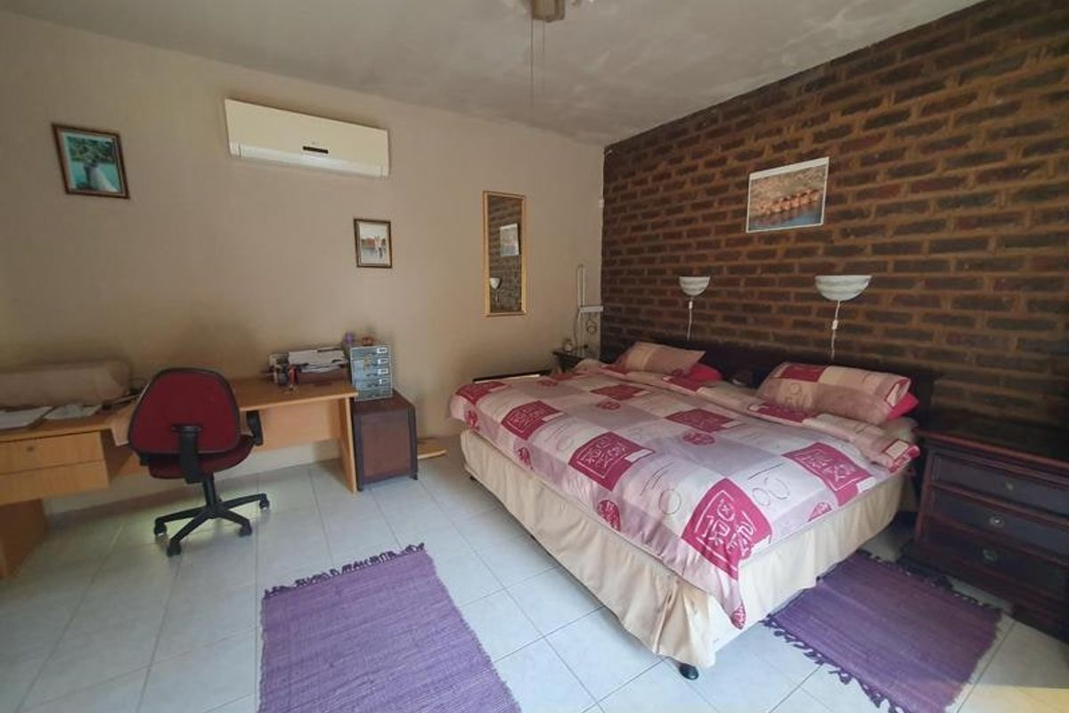 Spacious bedroom featuring an exposed brick accent wall, tiled flooring, and a wall-mounted air conditioning unit.