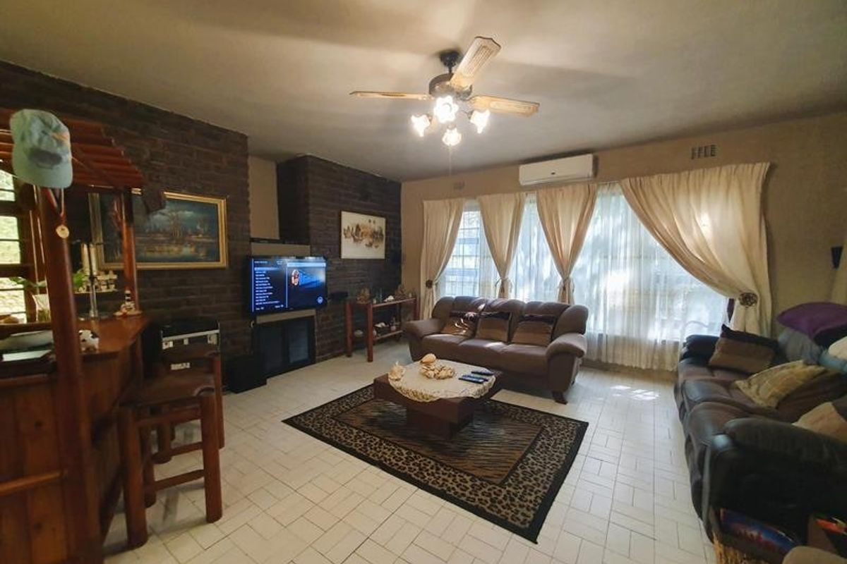 A living room featuring exposed brick walls, tiled flooring, a ceiling fan, and a wall-mounted air conditioning unit.
