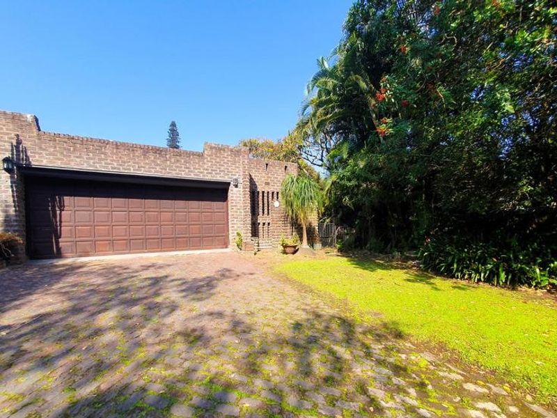 Front exterior view of the property featuring a brick facade, double garage, and a cobblestone driveway surrounded by mature garden landscaping.