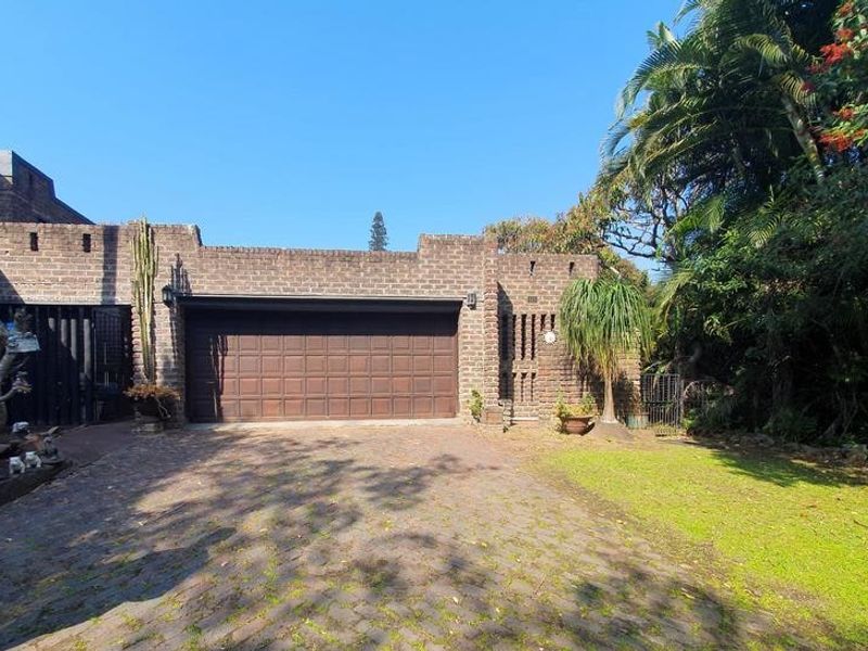 Front view of the property featuring a brick facade, a double garage door, and a paved driveway surrounded by established garden greenery.