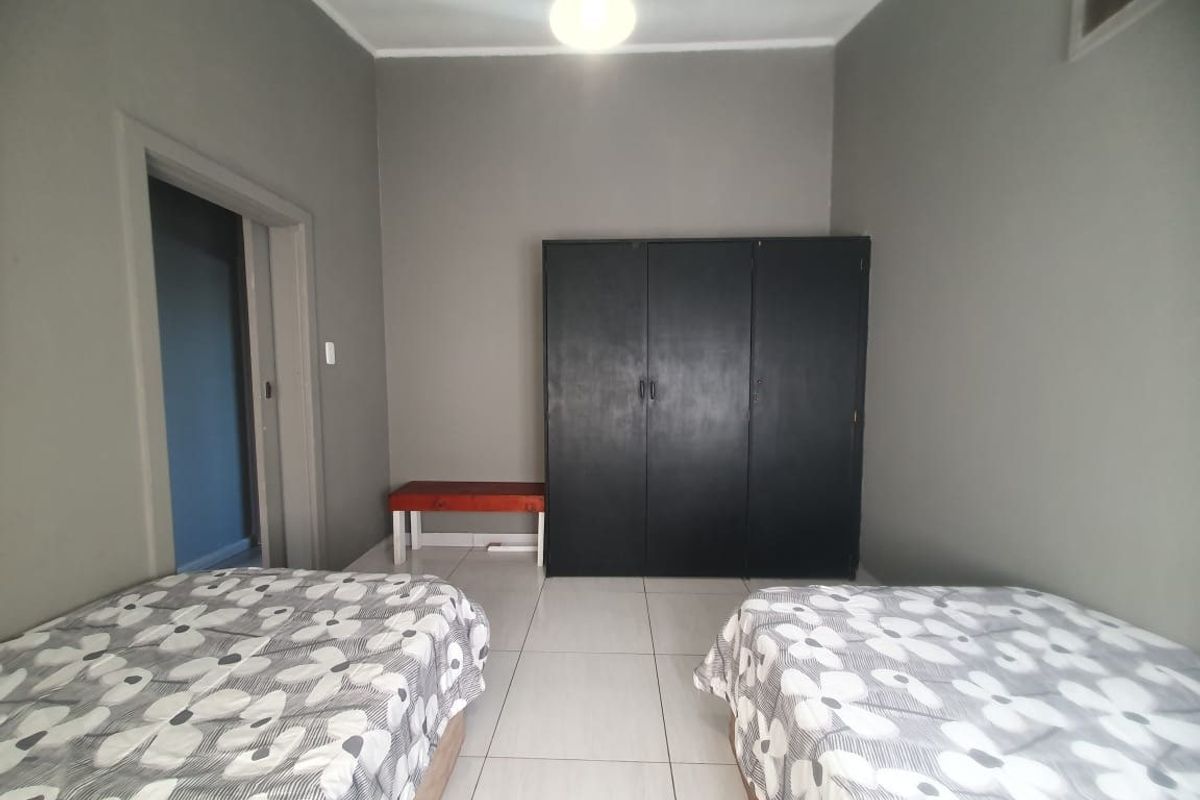 A bedroom featuring neutral grey walls, tiled flooring, and a built-in black wardrobe, offering a functional and clean living space.