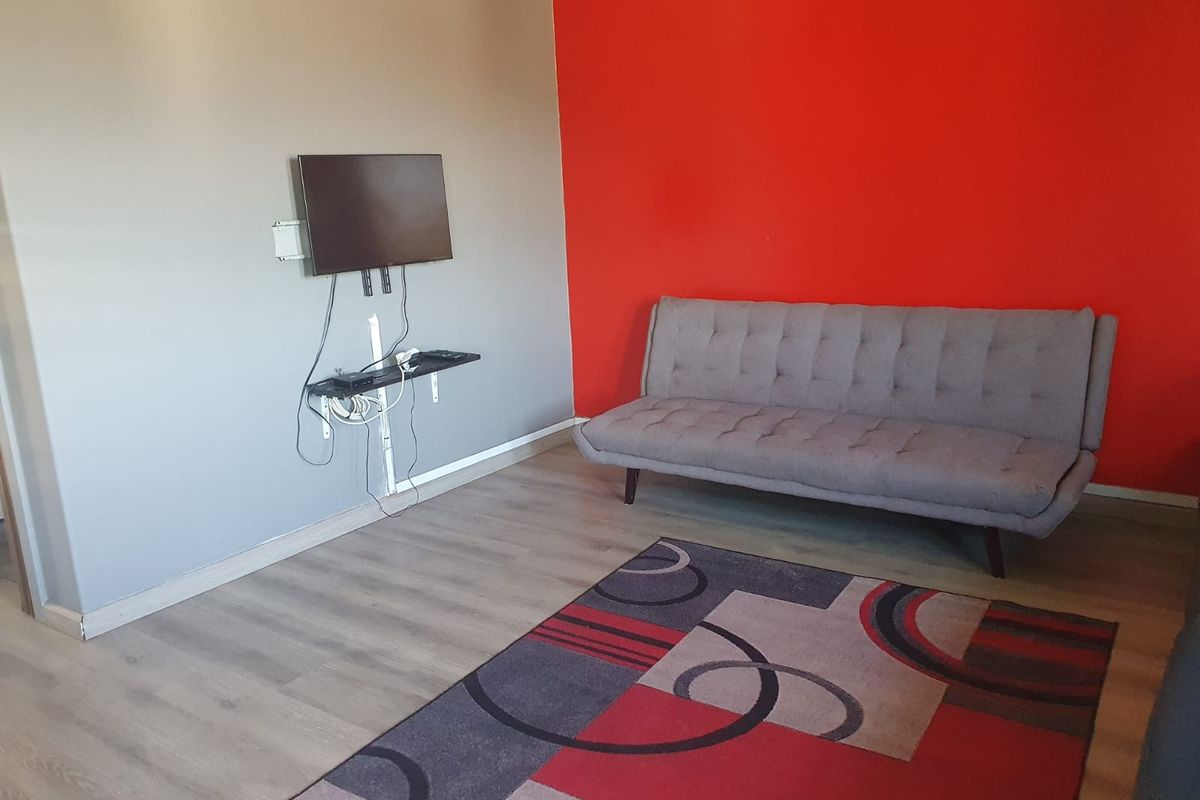 A living room featuring laminate flooring and a bold red accent wall, currently equipped with a wall-mounted television setup.