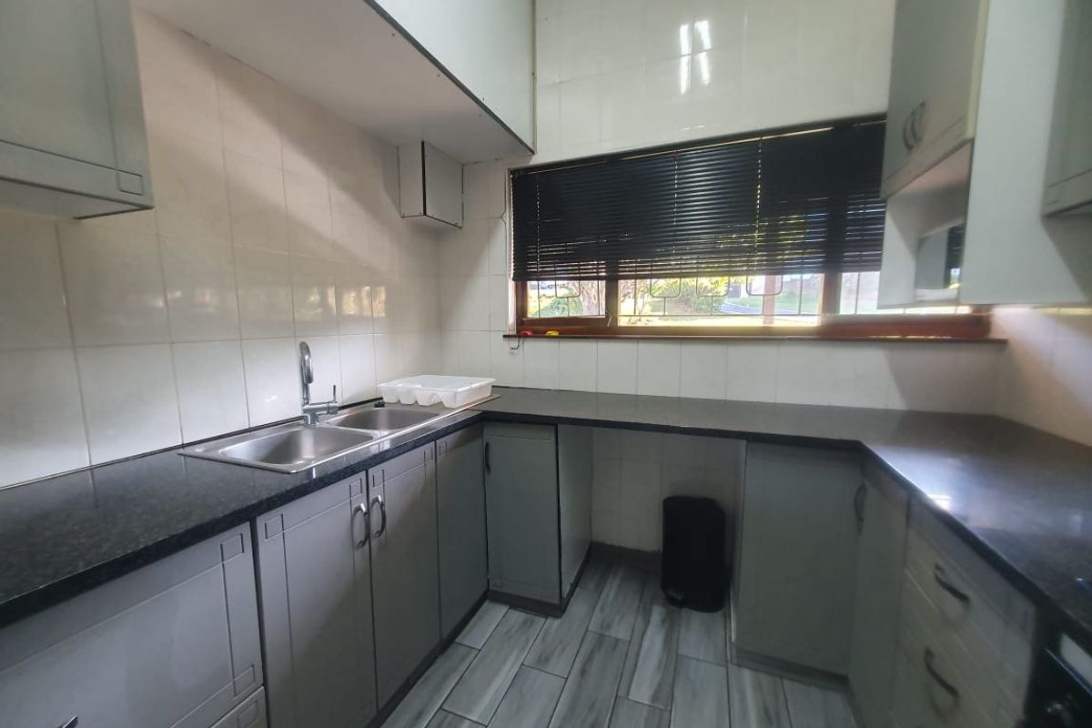 A functional kitchen featuring granite countertops, double basin sink, tiled backsplash, and ample built-in cabinetry with a neutral finish.