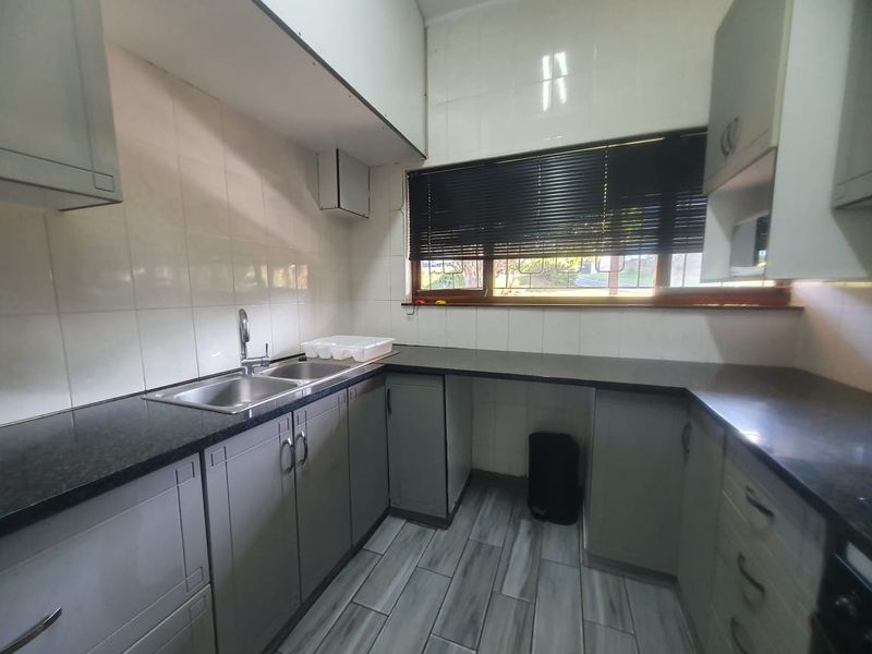 A functional kitchen featuring granite countertops, double basin sink, tiled backsplash, and ample built-in cabinetry with a neutral finish.